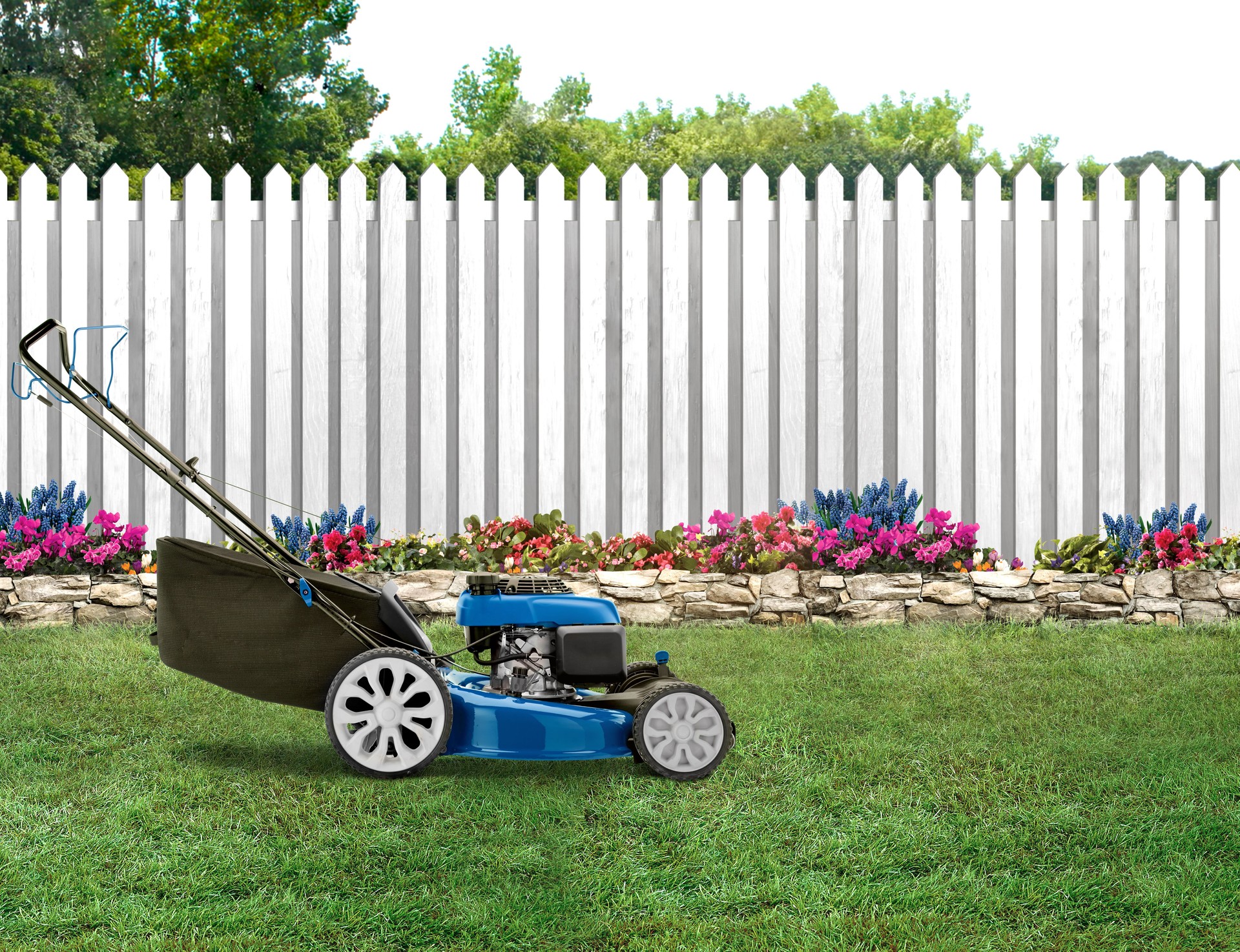 Blue lawn mower in a backyard with green grass and picket wood fence